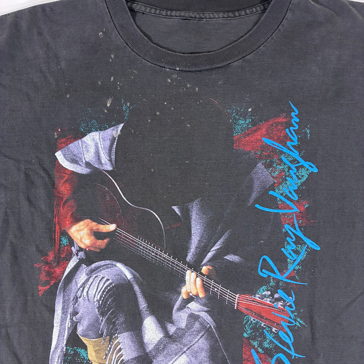 A faded black graphic t-shirt featuring a printed image of a person playing an electric guitar, with blue and orange script text reading 'Stella Ray Vaughan' and 'double trouble'.